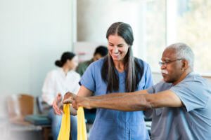 Therapist smiles as senior man learns to use elastic band during occupational therapy session